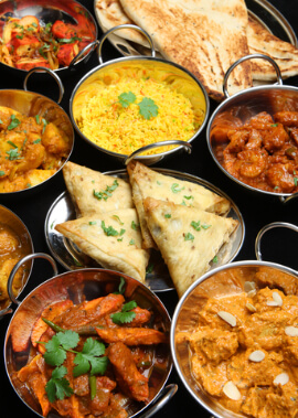 Indisches Curry-Bankett. Auswahl an indischen Gerichten, darunter Currys, Reis, Samosa und Naan-Brot