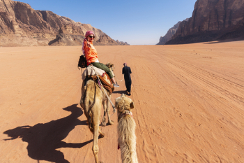 beautiful young woman tourist in white dress riding on camel